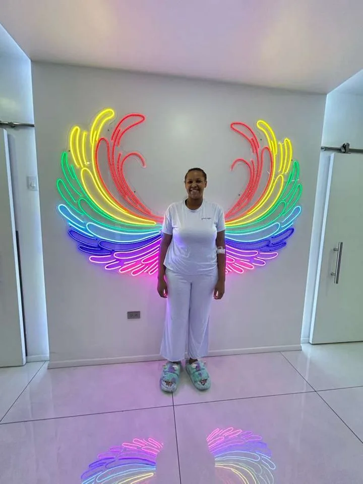 Patient smiling in front of a neon wings sign at the surgery center during her stay